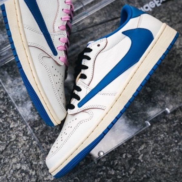 Pair of white sneakers with blue accents and contrasting lace colors (pink on left shoe, black on right) resting on a dark surface.