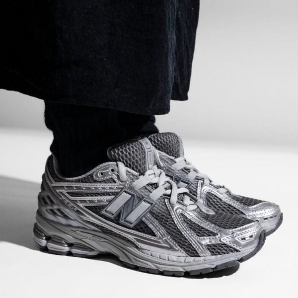 Gray athletic sneaker with a large N-shaped logo on the side, worn with black pants by a person standing.