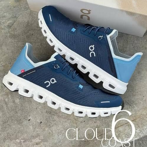 Two blue On Running Cloud sneakers with white segmented soles on concrete, with a box in the background.
