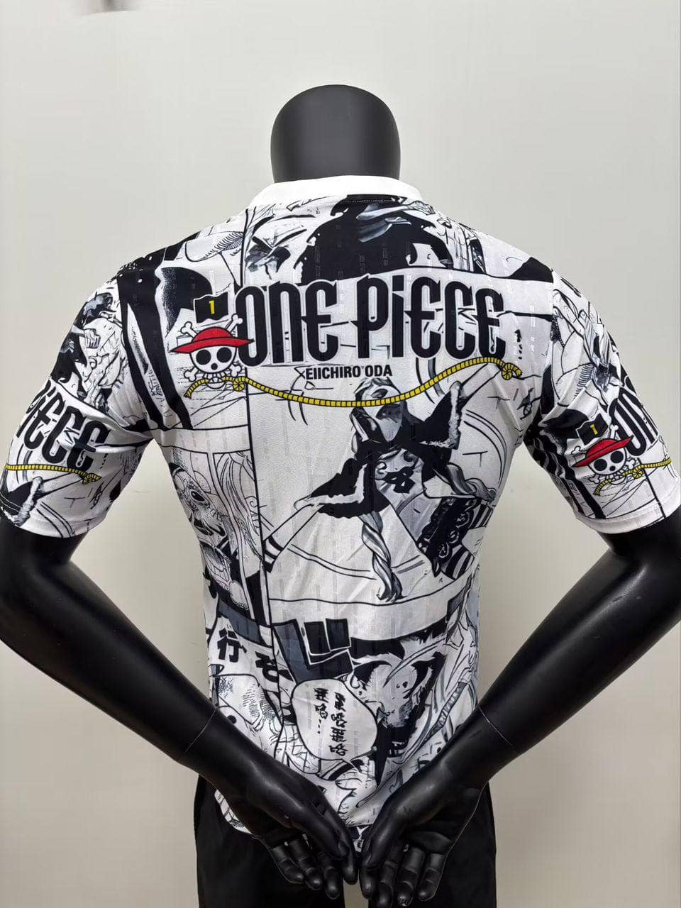 5418143704410689932 | AE JERSEY Back view of a white manga-themed shirt on a mannequin, covered in black-and-white One Piece panels with the text 'ONE PIECE' and 'EIICHIRO ODA'.