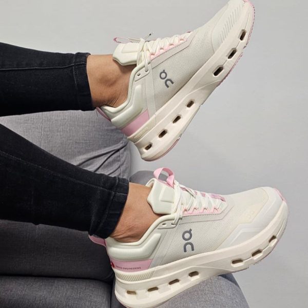 Cream running sneakers with pink laces and heel accents, On logo visible.
