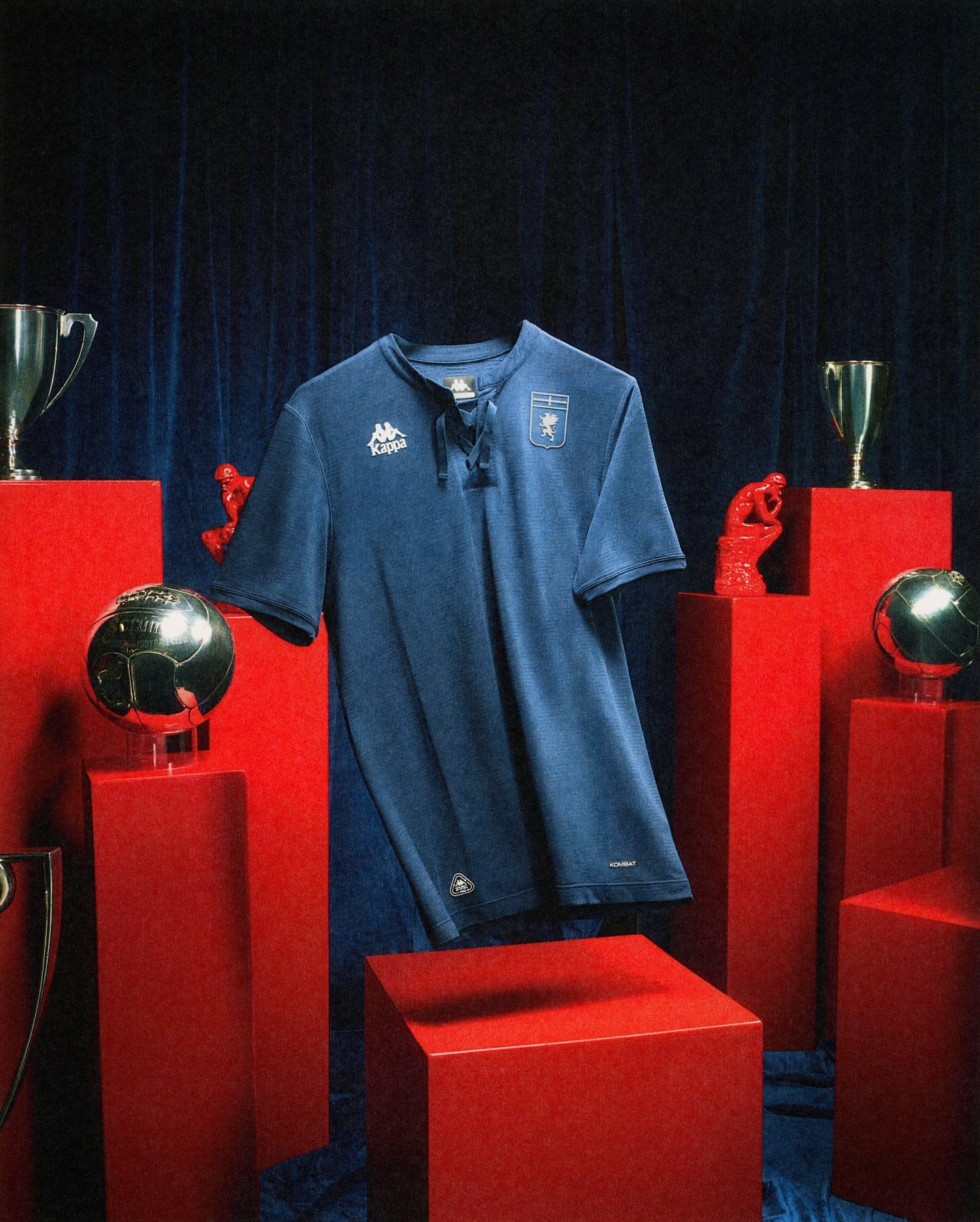 542046443_18528305527053657_5285735638079677977_n | AE JERSEY Blue sports jersey on a display stand surrounded by red pedestals and trophies against a dark backdrop.