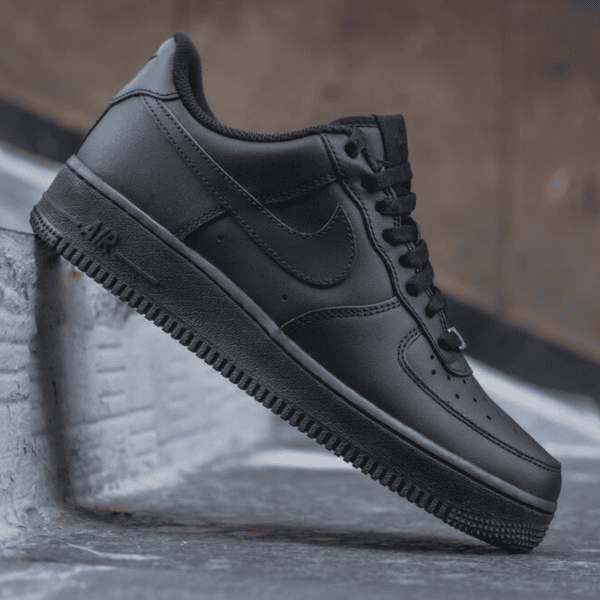 Black Nike Air Force 1 sneaker perched on a concrete step, showing the side and sole with the Nike Swoosh