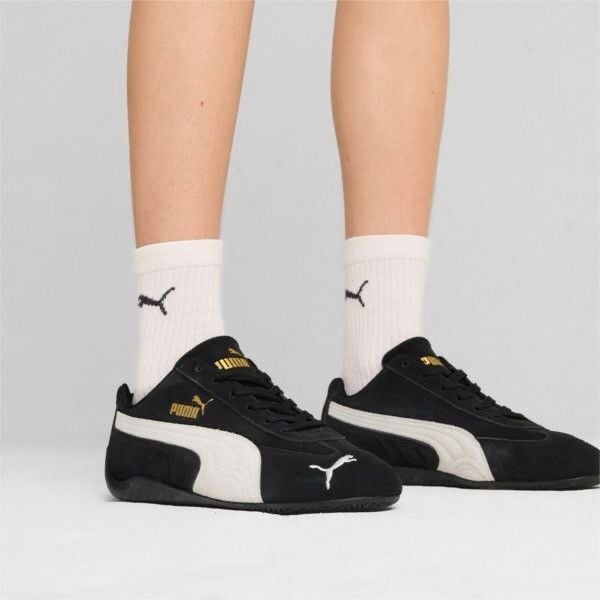 Person wearing white Puma socks and black Puma sneakers with white soles, shown from the ankles down.