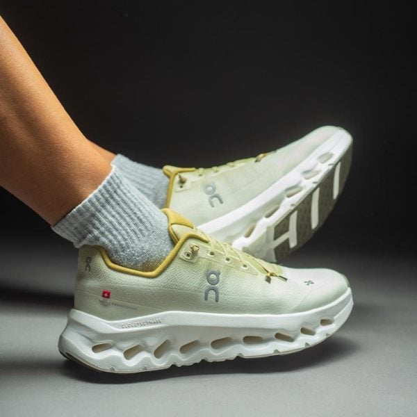 athletic runner's light-green sneakers with yellow trim and gray socks, mid-run on a dark background