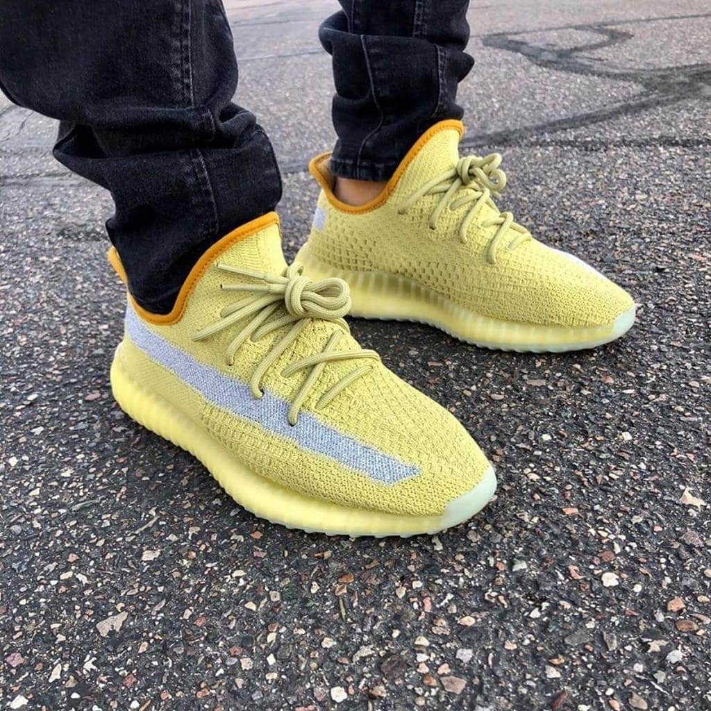 5d2d5435-76cf-4628-a477-4774e99b00df_23d9efd4-781c-475d-befb-e2341da0a3ec | AE JERSEY Yellow knit sneakers with a pale gray stripe, worn by someone in dark jeans on asphalt.