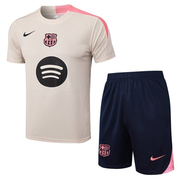 Beige FC Barcelona soccer jersey with pink shoulder detail and navy Nike swoosh, large circular sponsor logo, paired with navy shorts featuring the pink Barça crest.