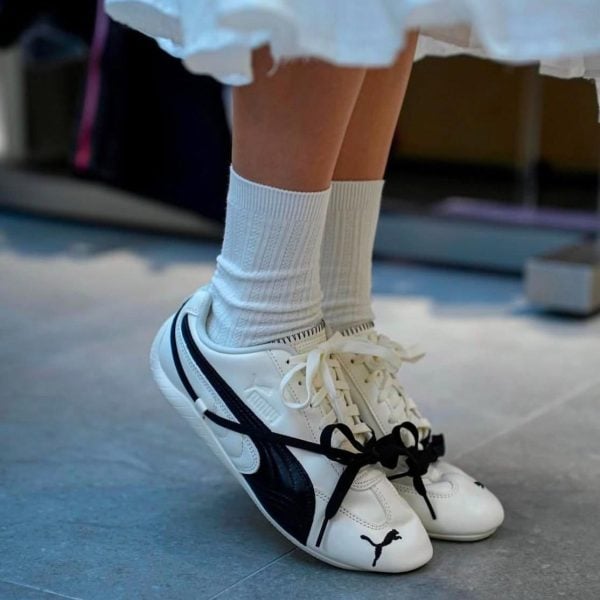 Child wearing white crew socks and white Puma sneakers with black stripes on a blue floor.