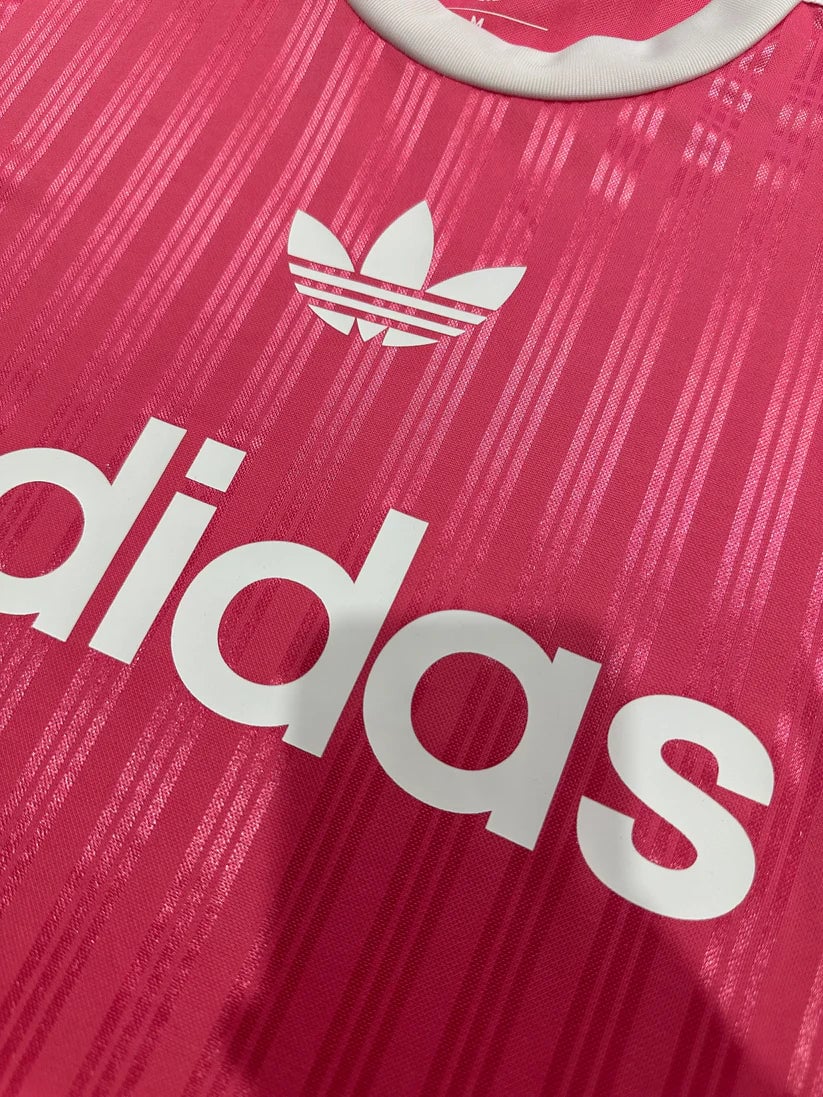 60b67fcd | AE JERSEY Close-up of a bright pink Adidas jersey featuring the white trefoil logo and part of the bold white adidas text.