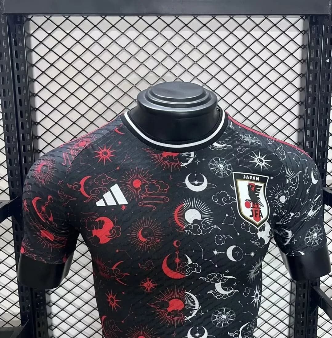 6183f50516ed4650 | AE JERSEY Black Japan national football team jersey on a mannequin, with a white Adidas logo and JFA crest, featuring a red and white celestial sun and moon pattern across the fabric.