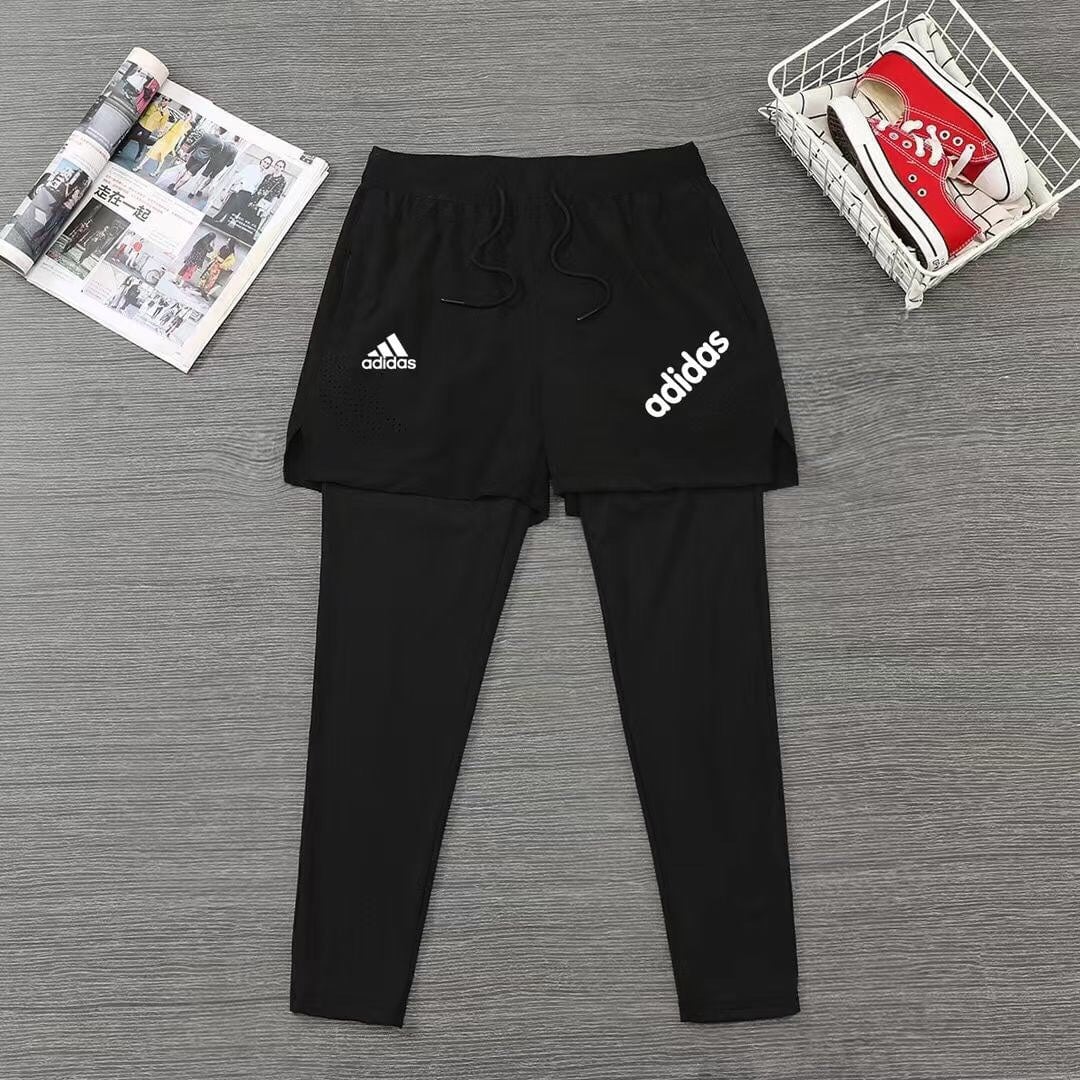 62df6aac_1 | AE JERSEY Black Adidas shorts layered over black leggings with logos visible on a gray wooden floor.