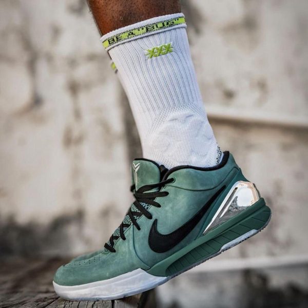 Close-up of a mint-green high-top Nike basketball shoe with a black swoosh, worn with a white sock featuring yellow-green accents, on a wooden surface.