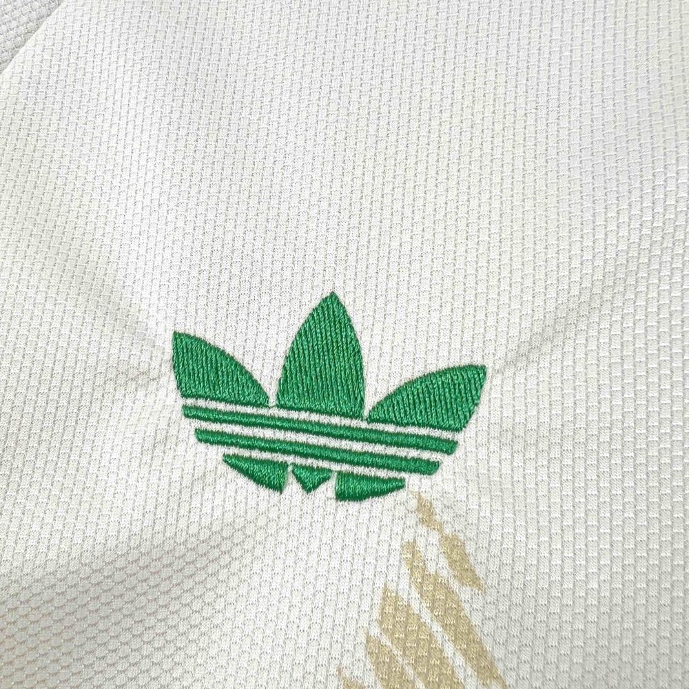 651477C6-1802-4A28-BF3B-9D16791BA886 | AE JERSEY Close-up of white textured fabric featuring a green Adidas trefoil logo embroidered on the material.