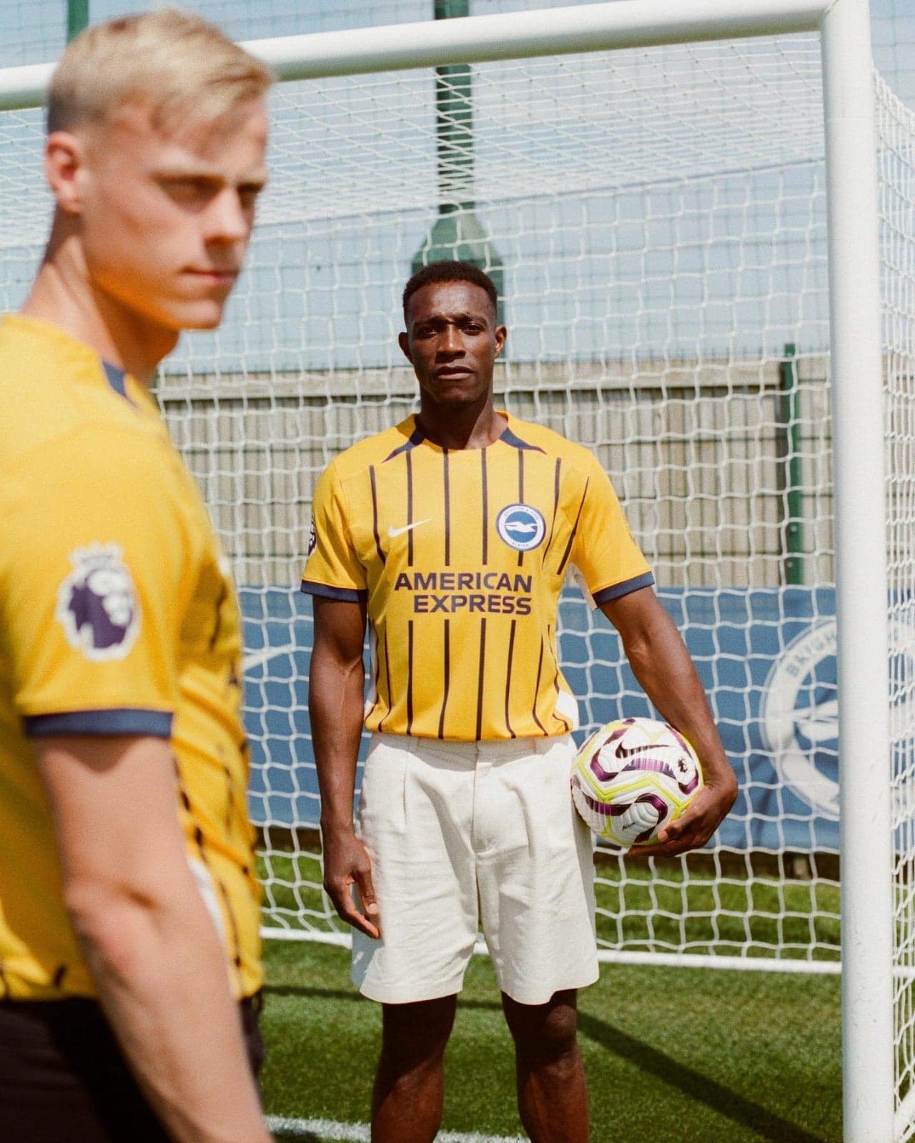 6EwqIY3iBOLOWXK | AE JERSEY Soccer players in yellow striped jerseys near a goal; the central player holds a ball, sponsor logo reads 'AMERICAN EXPRESS' visible on his chest.