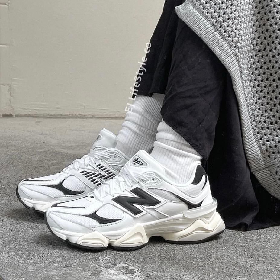 6ab11046-452d-4b81-9c40-06fd07588953_b3d61aba-baee-441d-81b6-6480ede057c9 | AE JERSEY Pair of white chunky sneakers with black detailing and white crew socks resting on a concrete floor beside a grey knit garment.