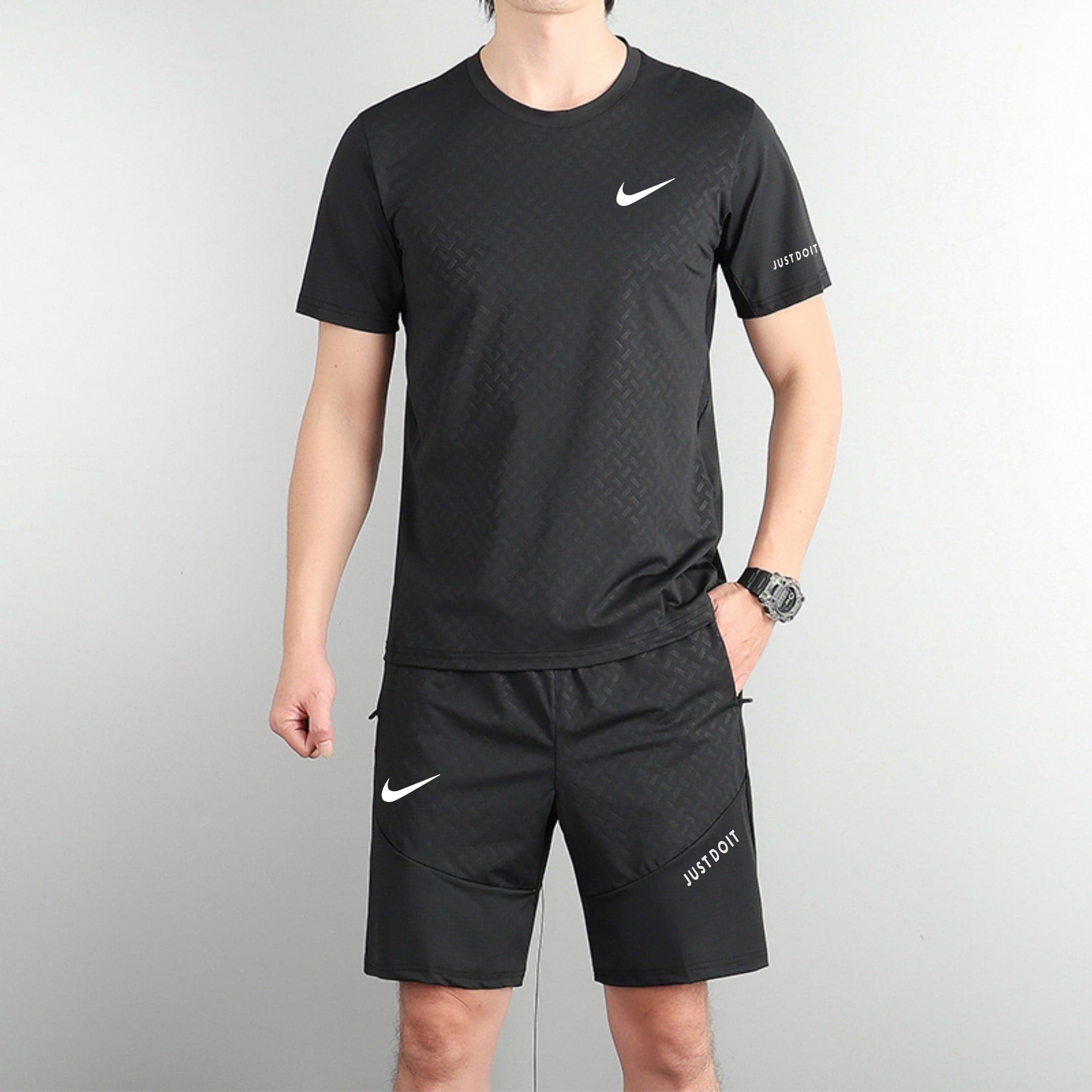 6cf89af7 | AE JERSEY Person wearing a black Nike athletic shirt with a white swoosh logo, standing against a light grey wall with matching black shorts featuring logos.