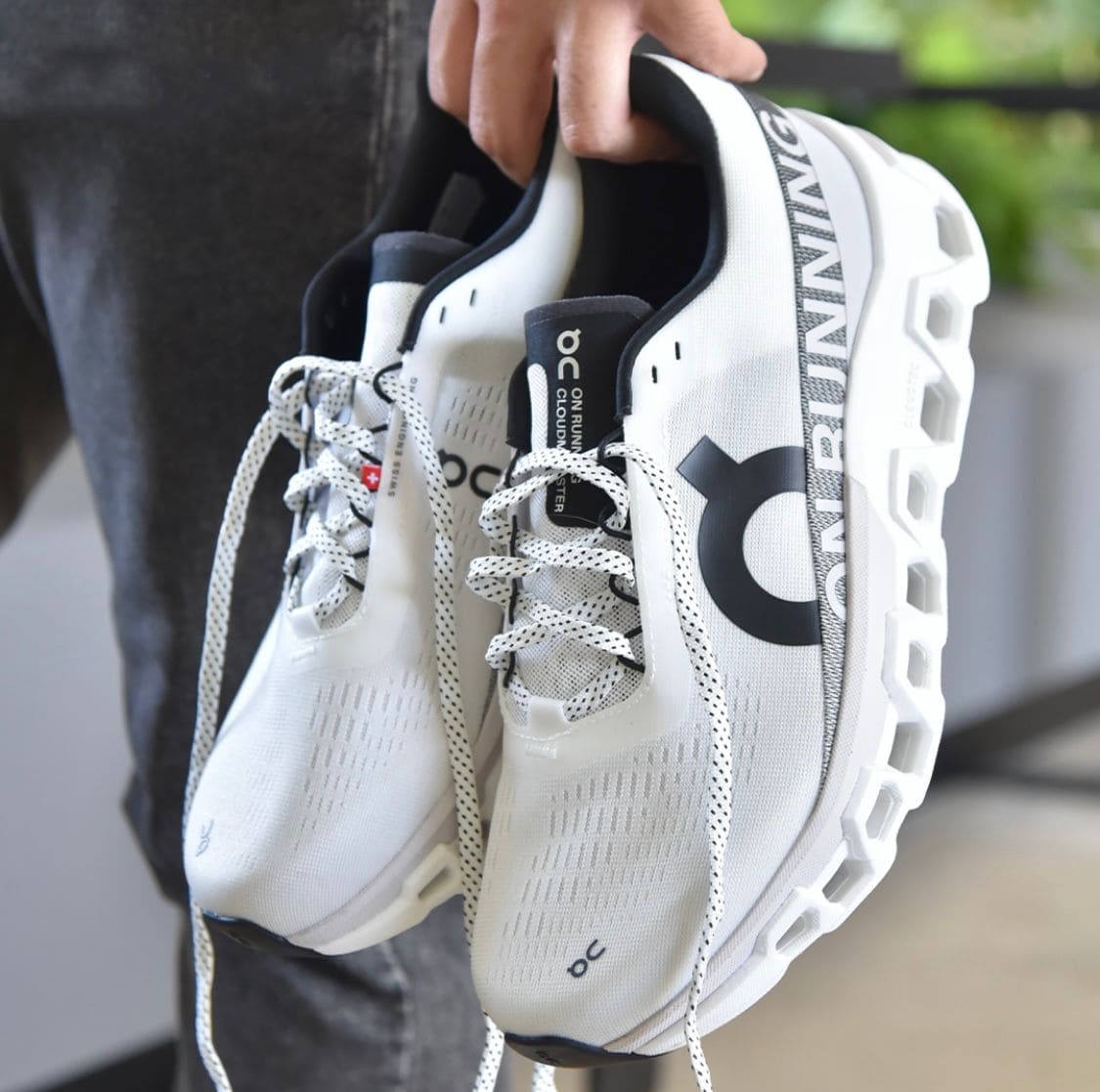 6dc5fcdc-1690-41fa-bb39-ca055869564d | AE JERSEY White On Running sneakers being held up, showing the textured sole and laces (close-up product shot).