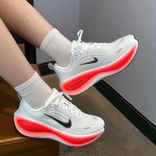 White Nike running shoes with black swoosh and bright red glowing midsole, worn with white socks by a person seated on a bench.