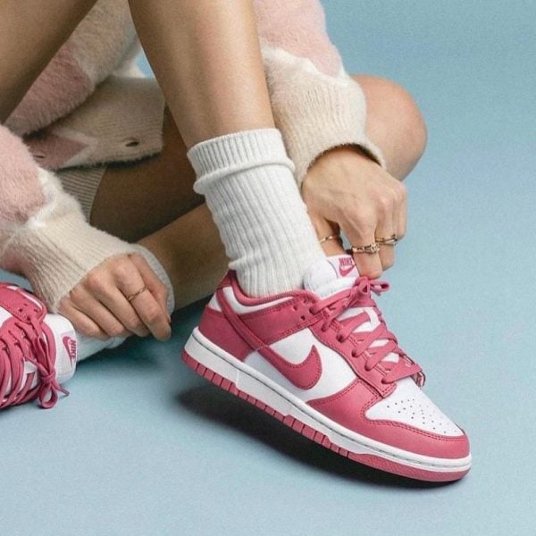 Close-up of a person tying pink and white Nike sneakers with white socks against a light blue background.