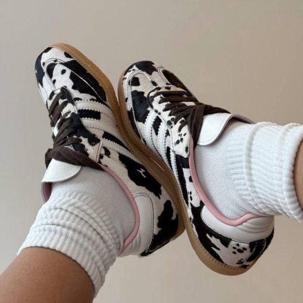 Twin cow-print sneakers with white socks, laid back-to-back on a light background, highlighting a playful footwear look.
