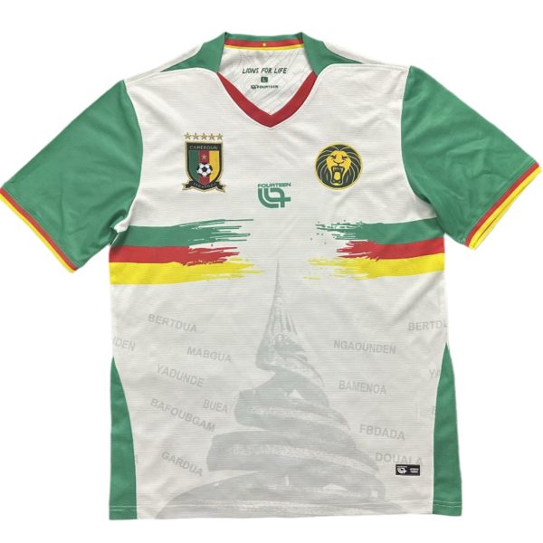 White soccer jersey with green sleeves and red-yellow trim, featuring Cameroon's crest and a yellow lion badge on the chest.