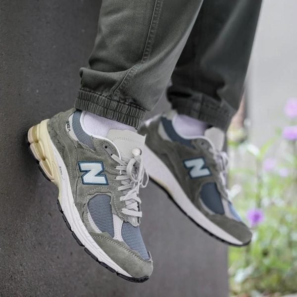 Pair of gray and blue New Balance sneakers resting on a ledge, showing the side N logo and chunky soles.