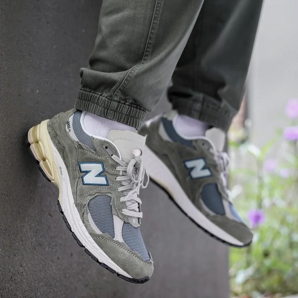 779aaf93-89d5-4277-bf3c-b0b5e71f0bc0 | AE JERSEY Pair of gray and blue New Balance sneakers resting on a ledge, showing the side N logo and chunky soles.