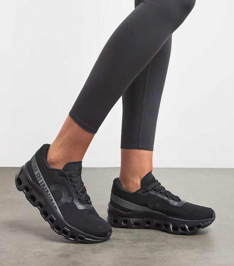 79285931-cc9b-43be-a4f5-48151ef57a1c | AE JERSEY Black athletic sneakers with a chunky hollow sole, shown with black leggings on a light floor; side view highlighting the elevated sole design.