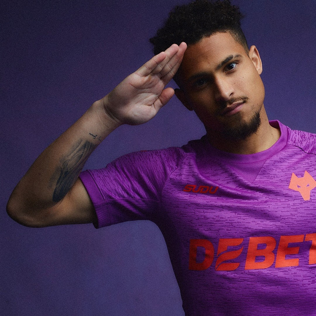 7NRxYniEWY6TsNs | AE JERSEY Man in a purple athletic shirt saluting with his right hand, looking at the camera; visible tattoo on forearm against a purple background.