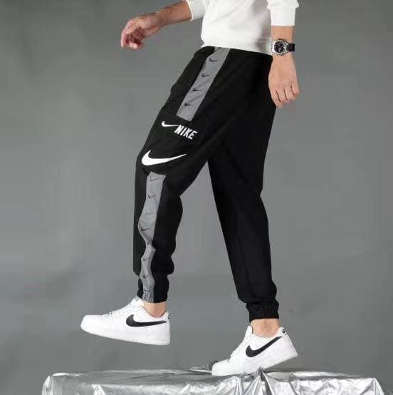 Person wearing black Nike joggers with gray side stripe and white Nike sneakers, stepping onto a platform.
