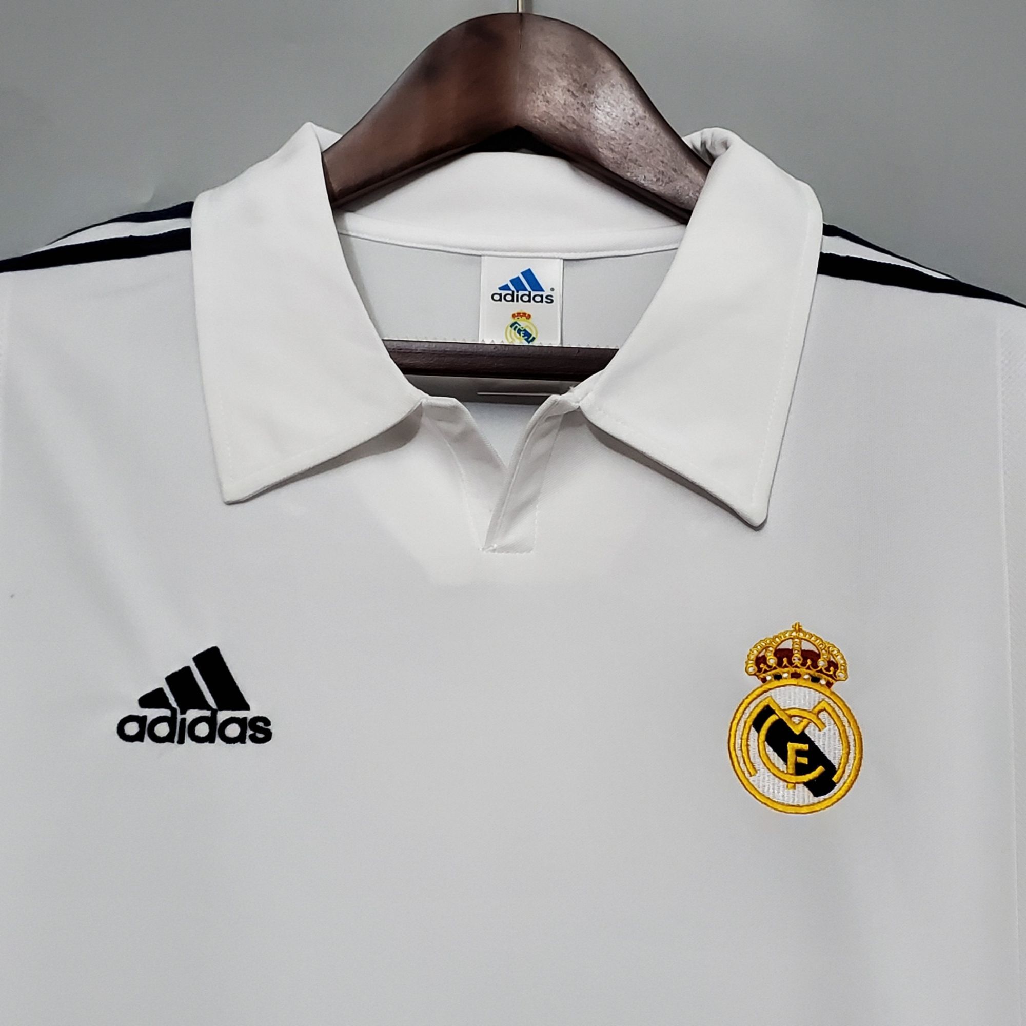 7df9d42e_41d364ac-d2a4-4cb0-be09-9369ae3195dc | AE JERSEY White Real Madrid football jersey on a hanger, showing the Adidas logo and club crest on the chest area.