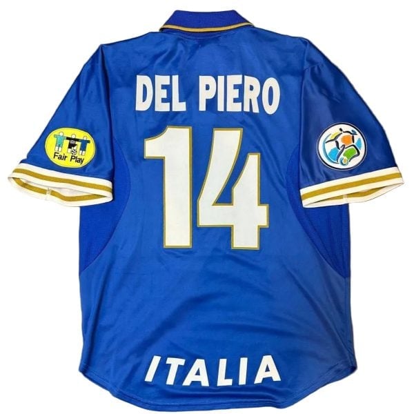 Blue Italy national team football jersey viewed from the back, showing the name 'DEL PIERO' and large number 14, with 'ITALIA' at the hem and patches on both sleeves (Fair Play on left, colorful emblem on right).