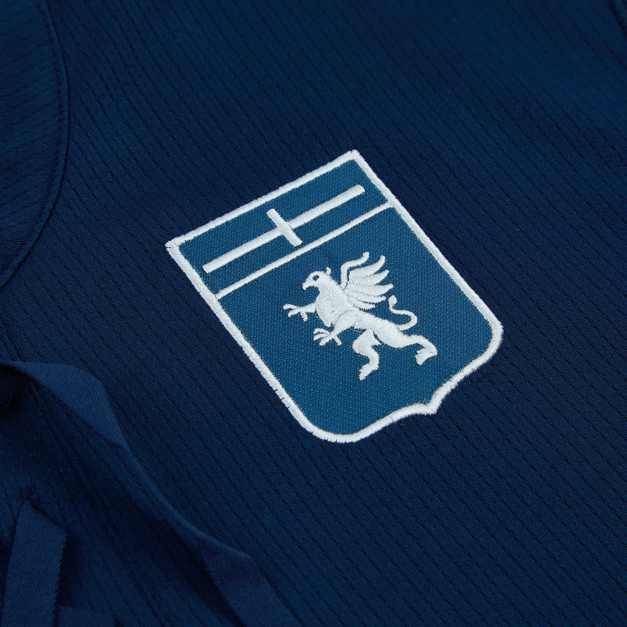 8056072326724-3_p8qvx8avcvrqcyzp | AE JERSEY Close-up of navy fabric with an embroidered patch: a blue shield featuring a white eagle outlined in white border.