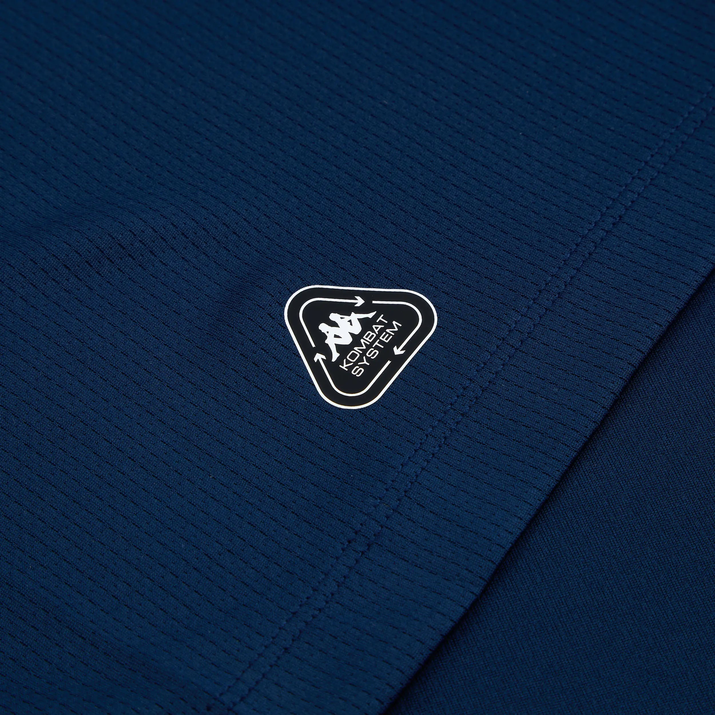 8056072326724-4_z3y9tyrys3ttjub1 | AE JERSEY Close-up of dark blue quilted fabric with a partial black shield-shaped patch showing a white border and unreadable text at the bottom edge and stitching nearby.