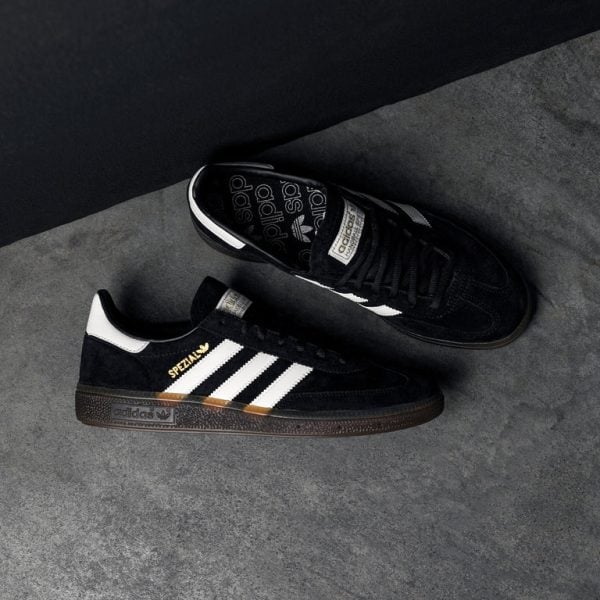 Black Adidas Spezial sneakers with white three stripes and brown sole on a gray surface, top view showing logo details for product photography