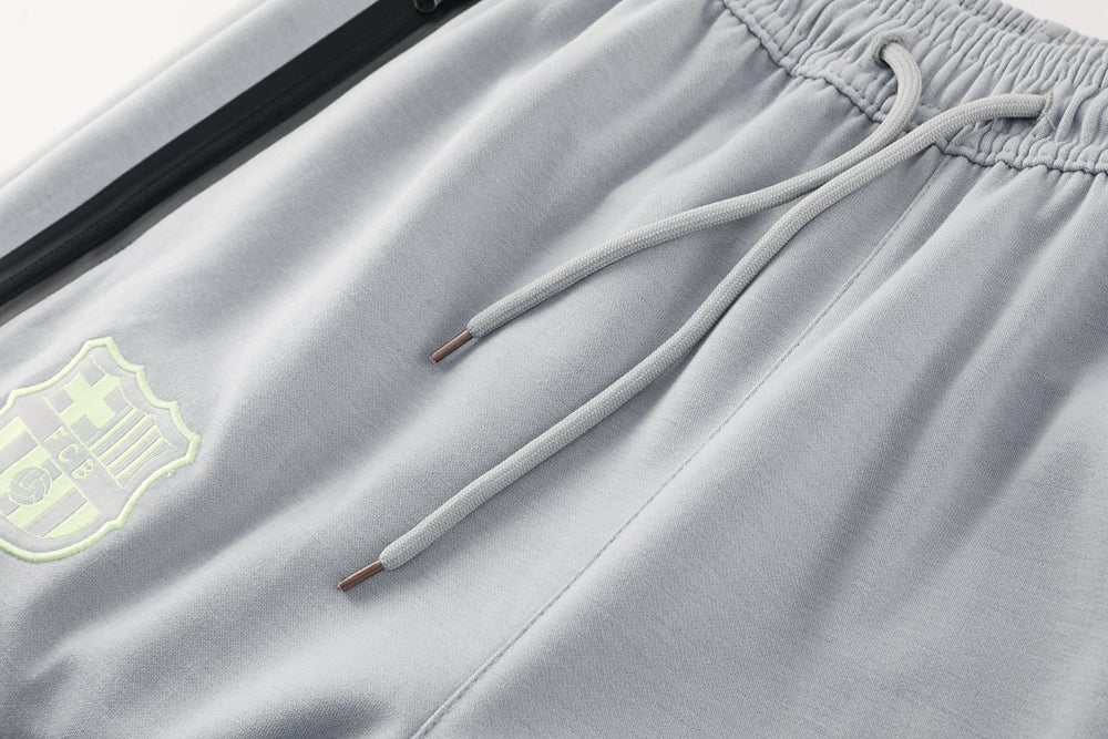 82997425 | AE JERSEY Close-up of light gray joggers showing drawstrings, elastic waistband, and a neon-green shield logo on the left leg/pocket area.