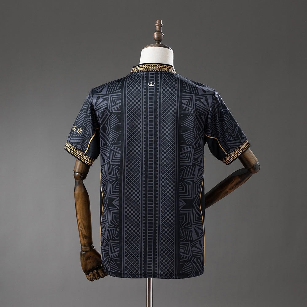 83a39f00 | AE JERSEY Back view of a navy short-sleeve shirt with geometric panels and gold piping on the cuffs, displayed on a dress form.