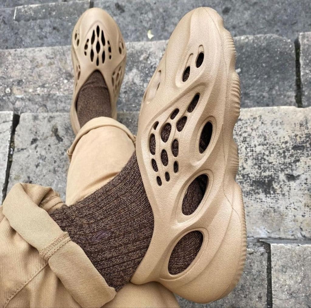8423ed3d-ef59-4ade-a9de-5321495db721_18f5d684-52f0-4e1f-8b77-f344cdab70cd | AE JERSEY Beige Crocs-style sandals with large cutouts on brown socks, resting foot on gray stone steps.