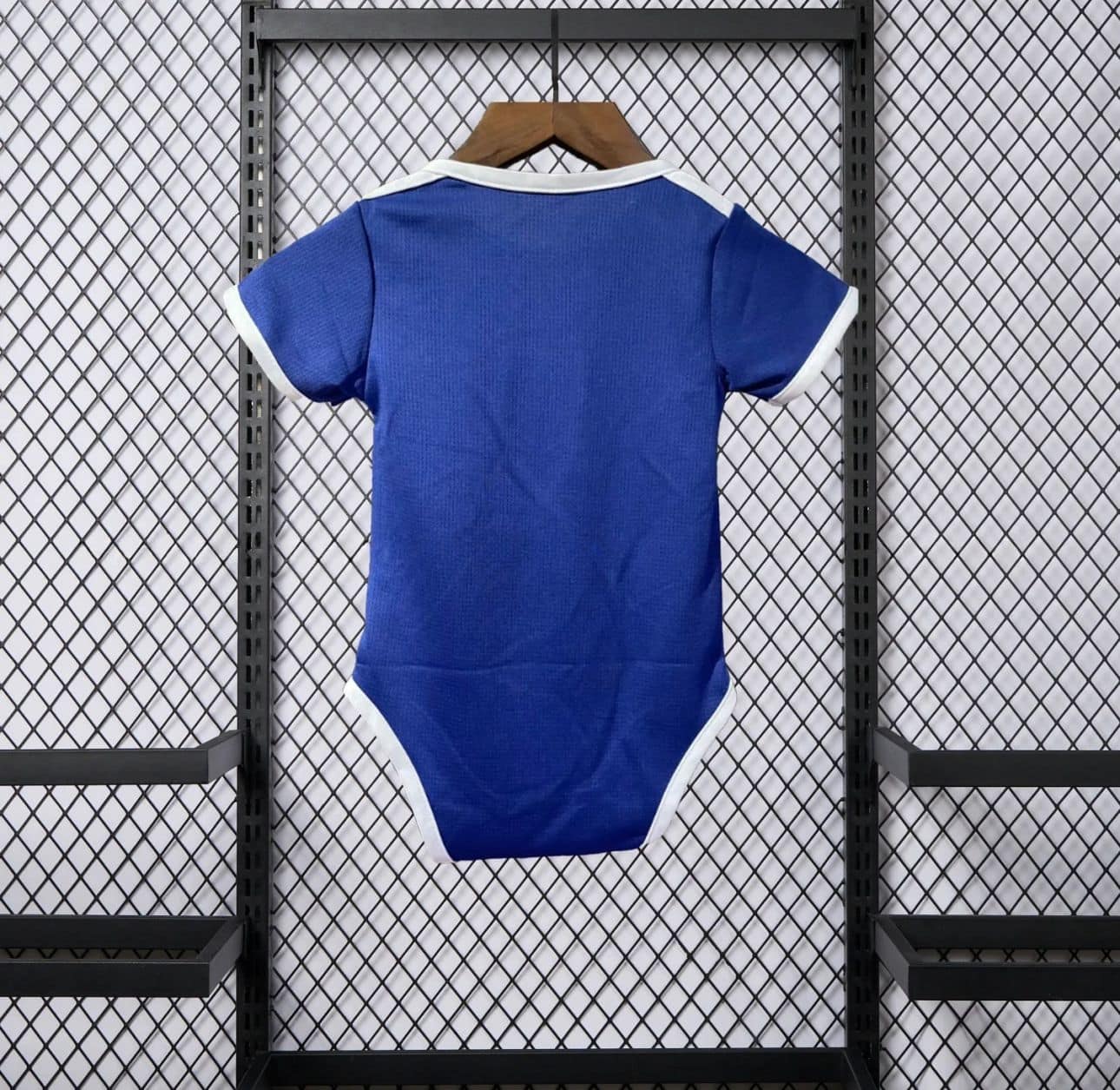 852794e4-8fac-439c-9b17-495d0926bb53 | AE JERSEY Blue infant onesie with white trim hanging on a wooden hanger against a metal mesh display backdrop