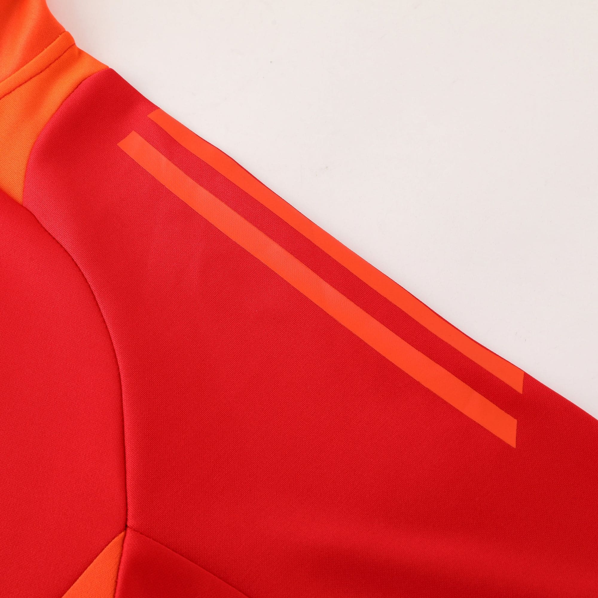 85806358 | AE JERSEY Close-up of red fabric with orange diagonal stripes on a garment, suggesting sporty outerwear detail.