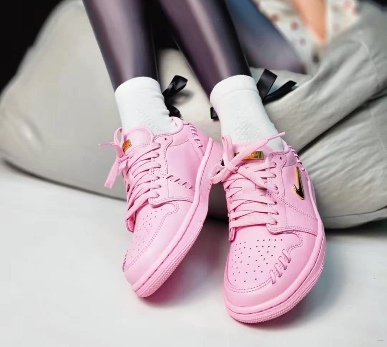 8618228e-e980-42da-a3fb-a6a003b901e7 | AE JERSEY Pair of pink sneakers with white socks resting on a light-colored sofa or chair cushion.