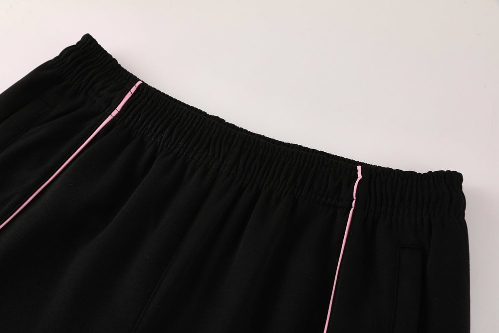 8940d585 | AE JERSEY Black elastic-waist pants with pink piping along the side seams and pockets, close-up view.