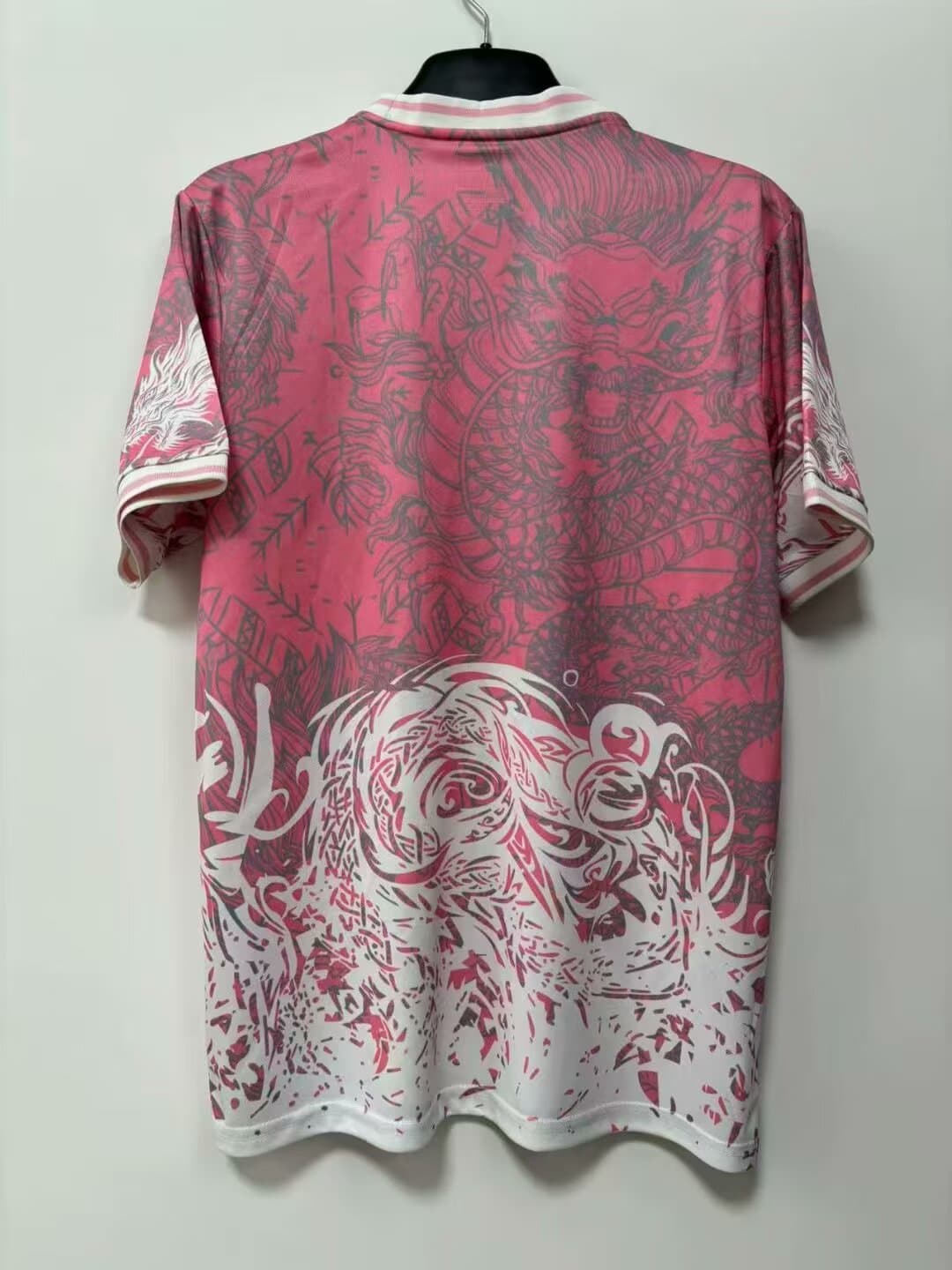 8d2557c1 | AE JERSEY Pink short-sleeve shirt on a hanger with white striped collar; features large gray dragon graphic across the back and a gradient fading to white at the bottom.