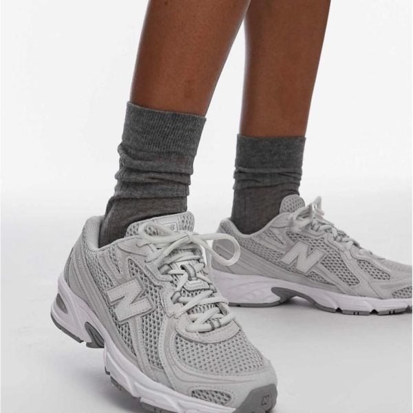 Person wearing gray crew socks and light gray athletic sneakers, standing with one foot forward.