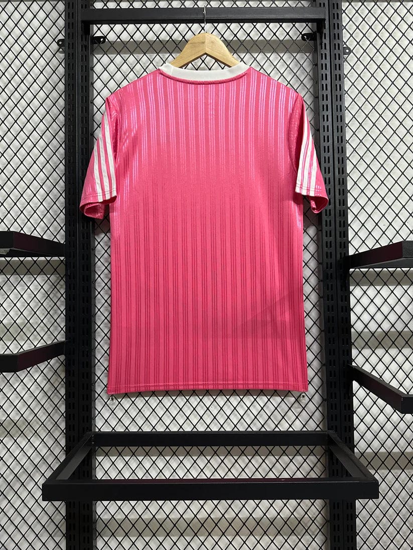 919fbad9 | AE JERSEY Bright pink striped T-shirt on a wooden hanger against a black grid display in a store windowed rack, showing vertical stripe pattern and white collar.
