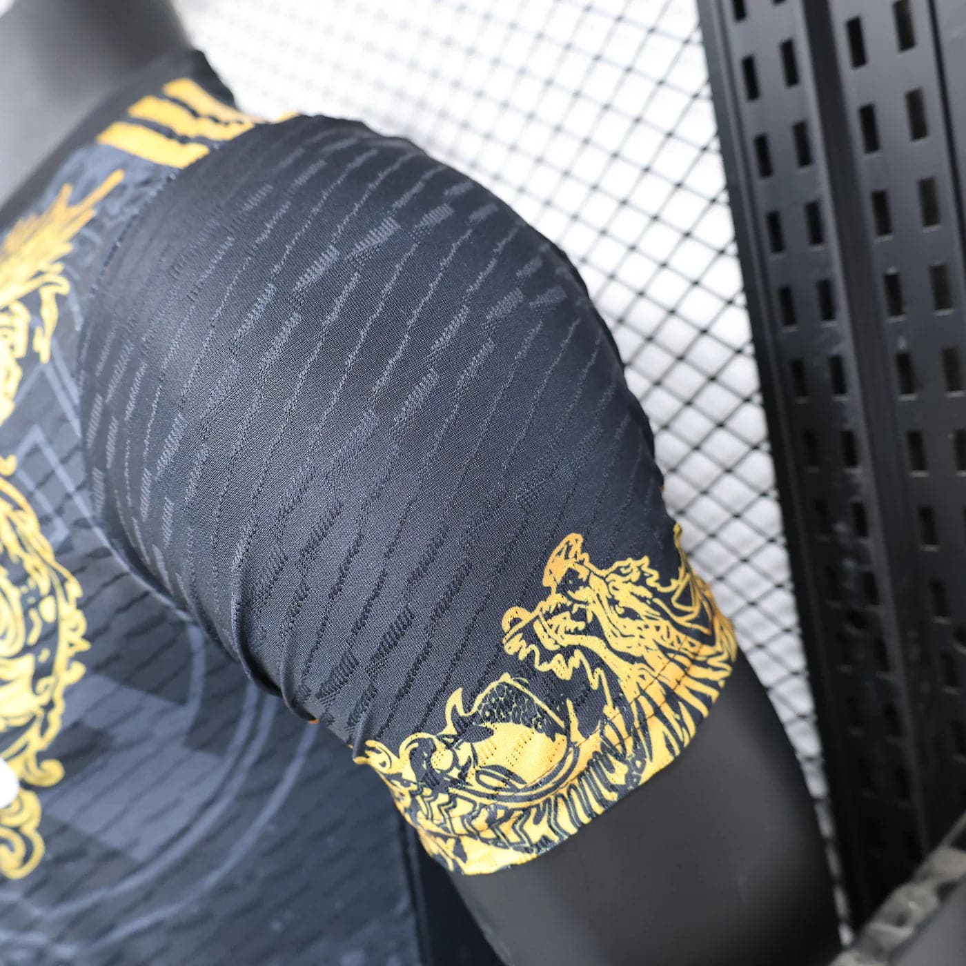 91c38c7d | AE JERSEY Close-up of a black athletic sleeve with subtle diagonal stripes and a yellow dragon graphic at the cuff.