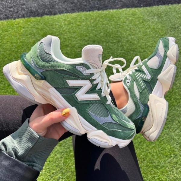 Green New Balance sneakers with white accents being held against a grass field backdrop.