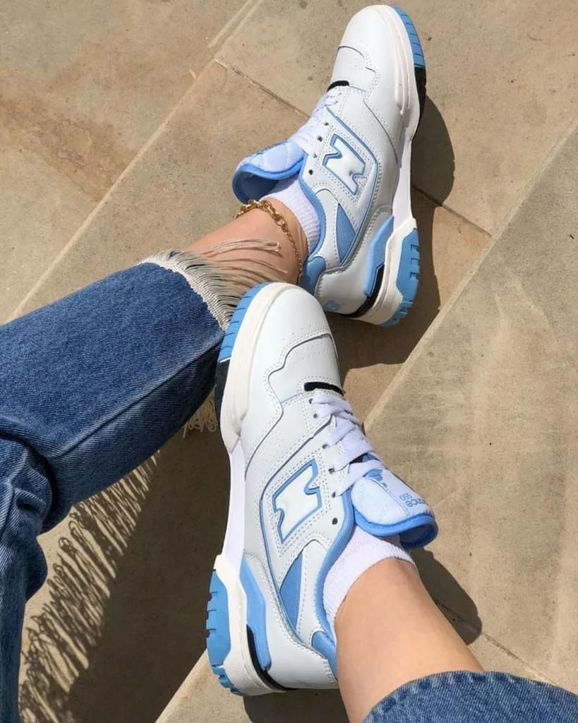 9b57824f-9eba-4c9e-b7fa-24843a50ab55_b73a0c64-18fe-4e6c-a8ba-6b98fab7462a | AE JERSEY White and sky-blue sneakers with chunky soles worn with ripped jeans, shown from above on a tan tiled surface.