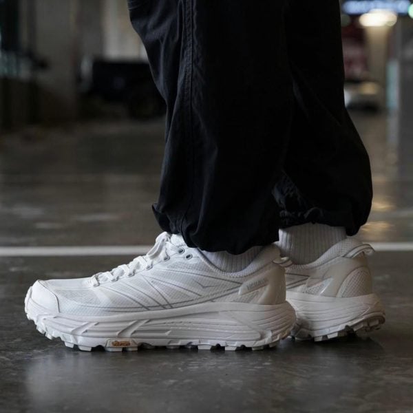White athletic sneakers with a chunky sole, worn with black joggers on a glossy floor.