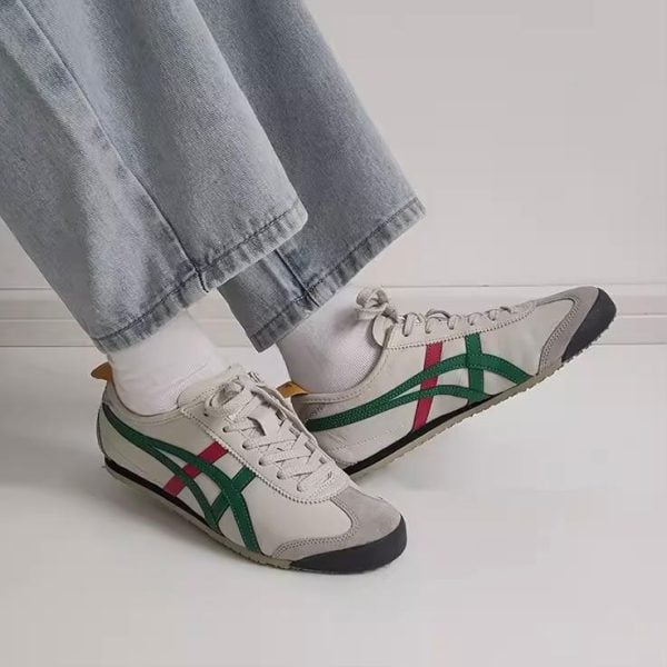 Person wearing white sneakers with green and pink stripes, standing on a white floor with light-wash jeans cuffed at the ankle